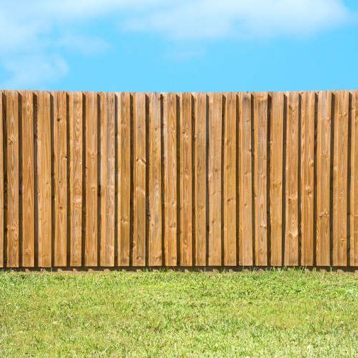 Generic wooden residential privacy fence with  a lush green grass yard in the foreground and a beautiful blue sky with fluffy clouds.